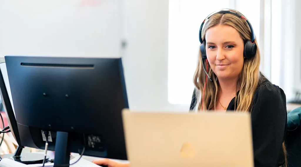 Person working at a desk with dual monitors and wearing headphones in a modern office setting.